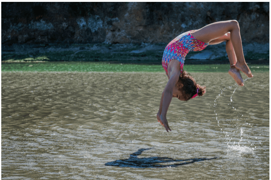 Mädchen springt ins Wasser, symbolisiert gesunde Entwicklung durch Bewegung und Vitamine für gesunde Entwicklung von Kindern.