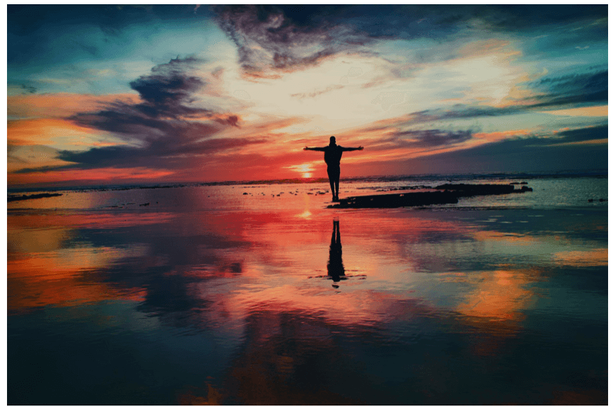 Silhouette of a person enjoying a colorful sunset by the water, symbolizing gesünder leben mit chronischen Krankheiten.