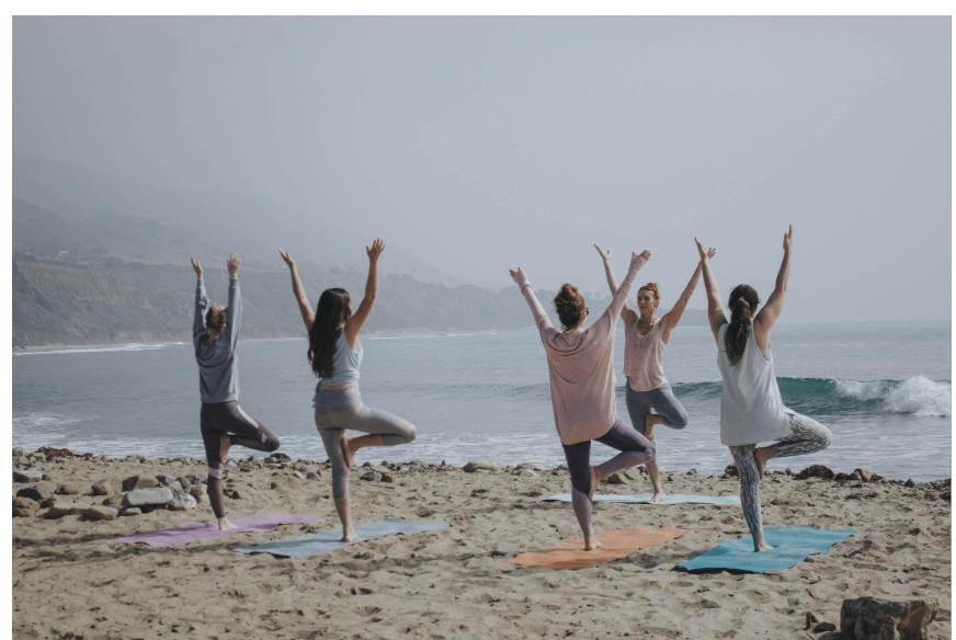 Gruppe von Frauen, die am Strand Yoga praktizieren, investieren in sich selbst durch Achtsamkeit und Fitness.