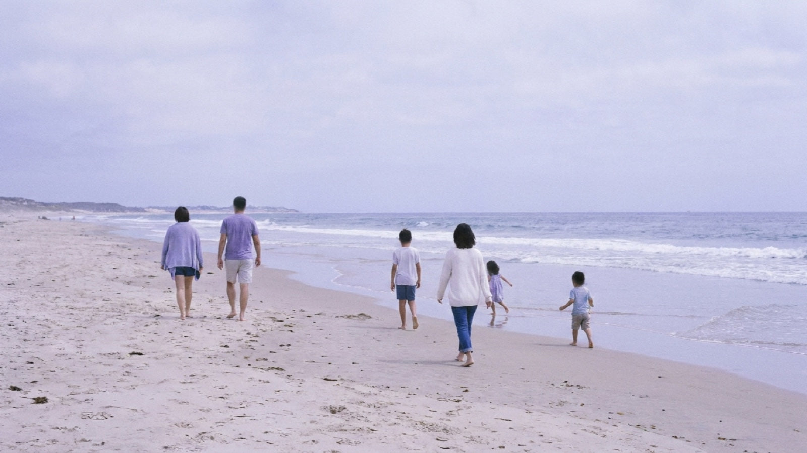 A family walking along the beach in calm weather, adults and children, seen from behind