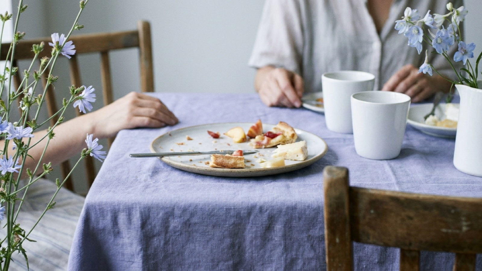 Zwei Menschen an einem gedeckten Frühstückstisch, halb geleerter Teller mit Brot, Käse und Obst