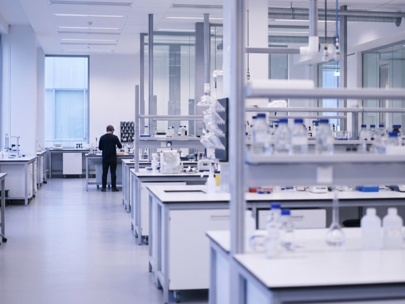 Blick in einen Laborraum mit Arbeitsplätzen, Laborgeräten und einer arbeitenden Person