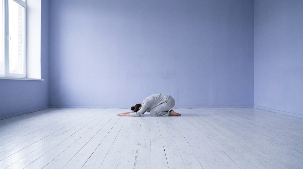 Person in einer nach vorn gebeugten Yogahaltung in einem leeren Raum